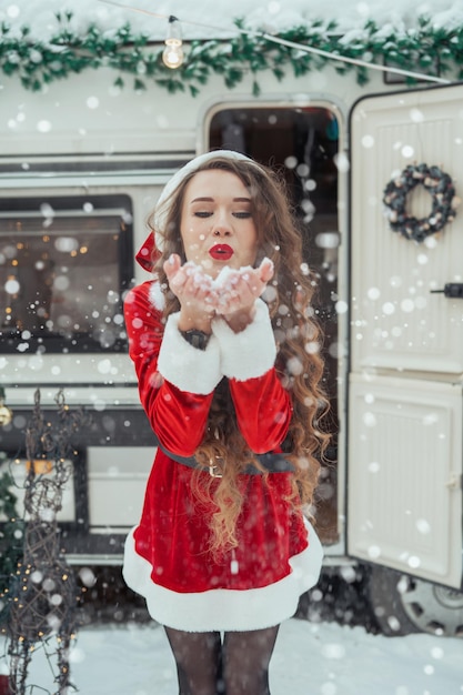 Young woman in santa costume decorates the christmas tree at winter campsite getting ready for the