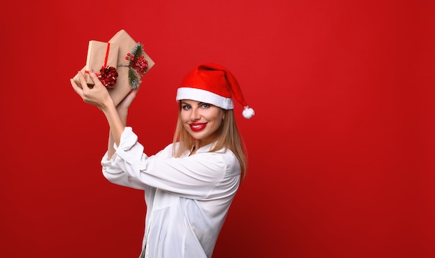 The young woman in a santa hat shows christmas presents rising and high.