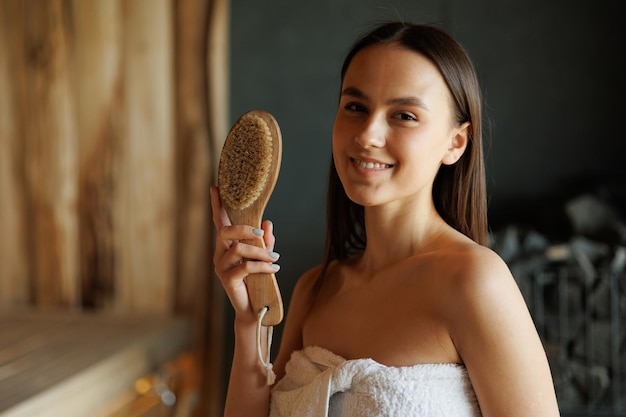 肌へのドライマッサージのためのブラシでサウナで若い女性