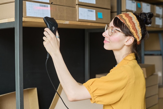 Young woman scanning parcels on shelf with scanner in warehouse