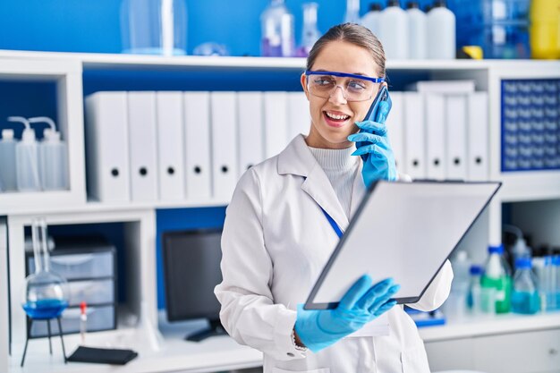 Photo young woman scientist talking on the smartphone reading document at laboratory