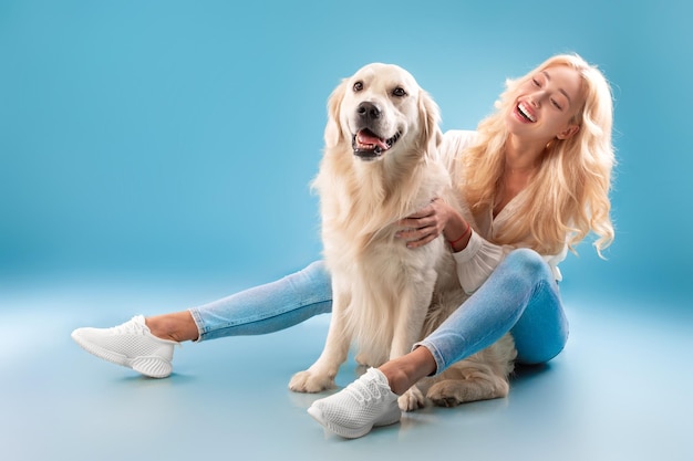 青いスタジオで彼女の犬を引っ掻く若い女性