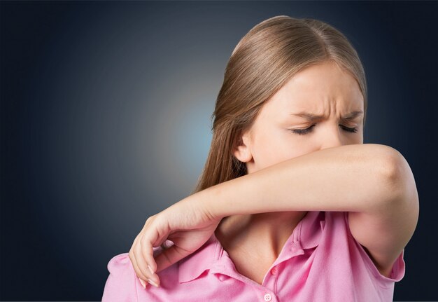 Young woman scratching her nose with elbow on dark gray background