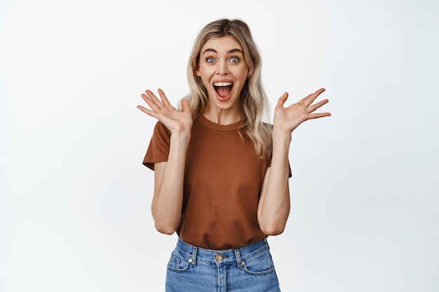 Young woman screaming and looking surprised excited about great news showing positive reaction to advertisement white background