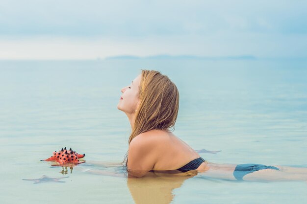 Young woman in the sea with red starfishes