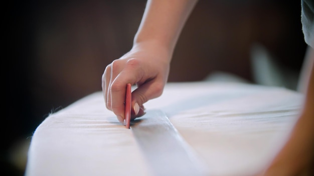 Young woman seamstress making marks using the soap and ruler on the cloth for cutting