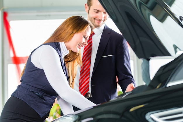 Young woman and seller with auto in car dealership