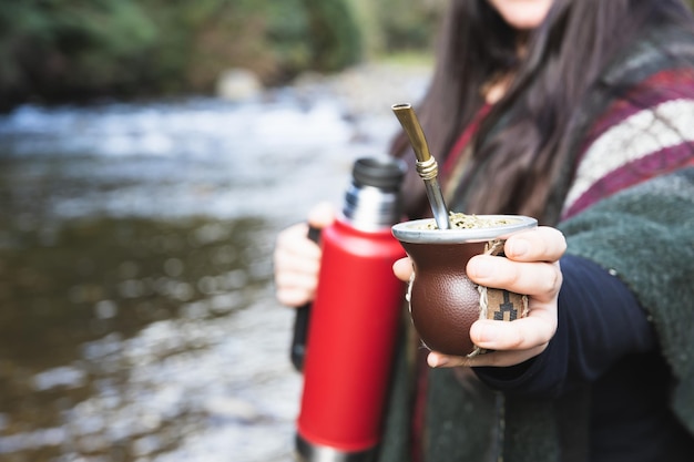 Young woman serving mate in a natural space Beside the river Latin beverage