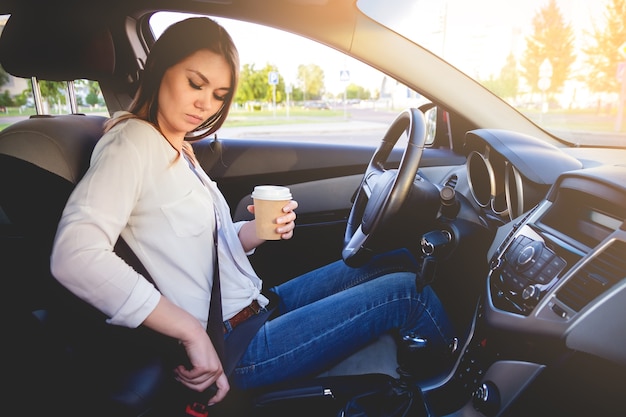 Young woman setting seat belt with a cup of coffee in hand