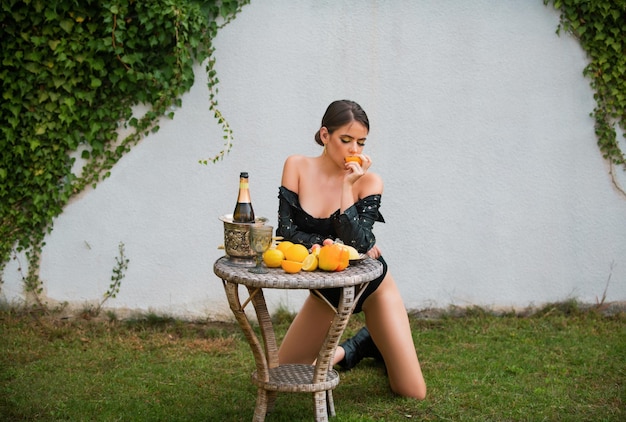 Young woman in sexy pose with fresh fruit on a wooden table in garden outdoors healthy vegetarian fo