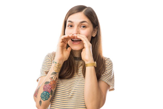 Young woman sharing secrets while covering mouth with both hands against white background