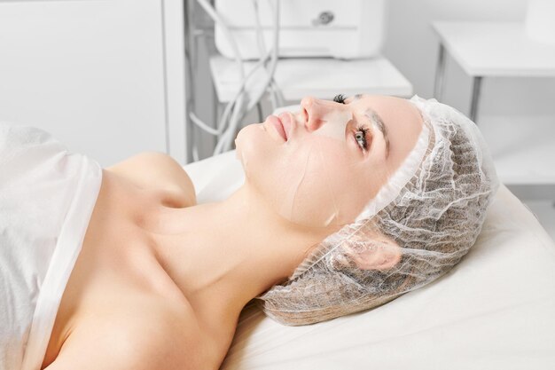 Young woman in sheet mask on face for rehydrate face skin anti wrinkles procedure in beauty salon