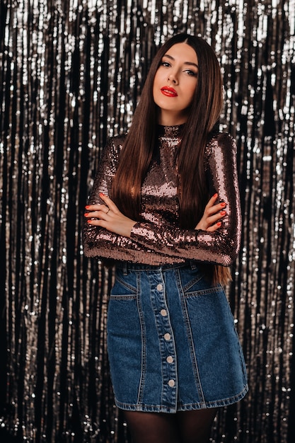 A young woman in a shiny jacket posing over silver tinsel curtain