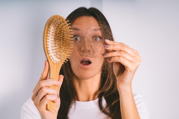 Young woman shocked because of hair loss problem Woman holding hair brush and showing damaged hair