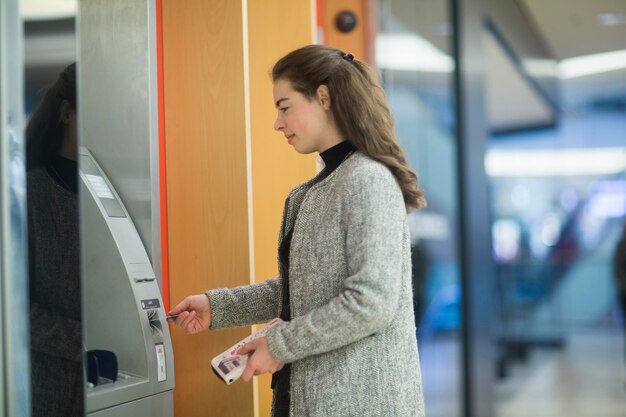 Photo young woman in a shopping mall using cash machine