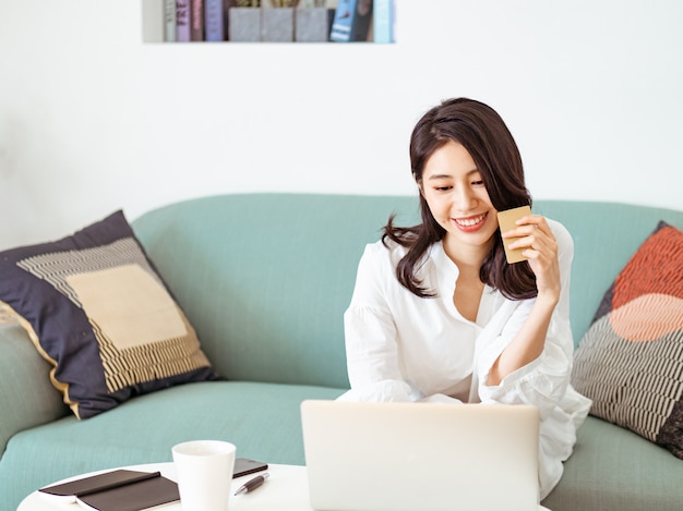 Giovane donna che fa shopping online con carta di credito e laptop a casa