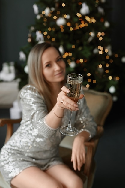 A young woman in a short dress keeps a glass of champagne and\
makes a cheers gesture