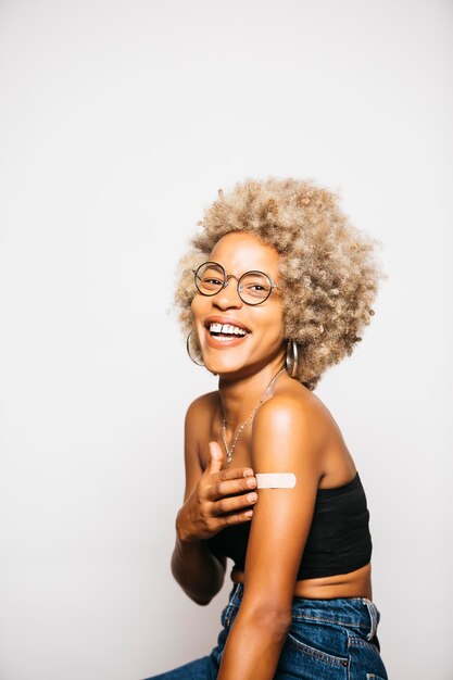 Young woman showing the bandaid on her arm after vaccination standing Against white background