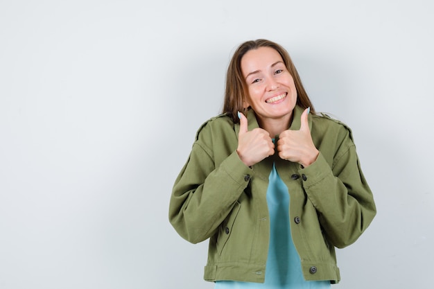 Young woman showing double thumbs up in t-shirt, jacket and looking jolly. front view.