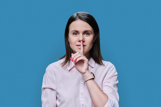 Young woman showing finger on lips gesture on blue background