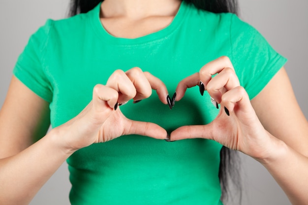 Young woman showing heart on gray background