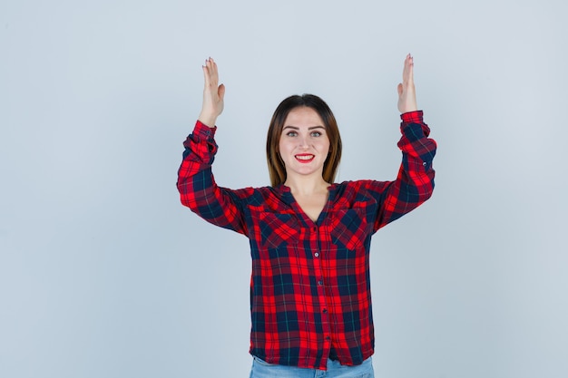 Young woman showing large size sign in checked shirt and looking jolly , front view.