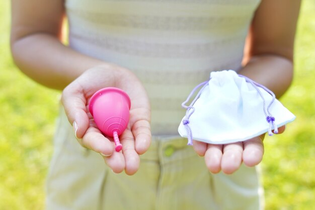 Young woman showing a menstrual cup with bag standing against green natural background