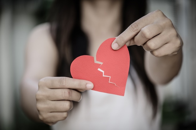 Young woman showing red ripped paper heart. Broken hearted concept.