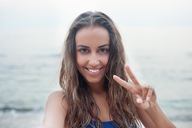 Young woman showing sign victory with fingers near the sea