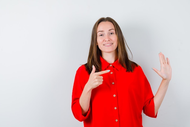 Young woman showing stop gesture, pointing to the side in red blouse and looking cute , front view.