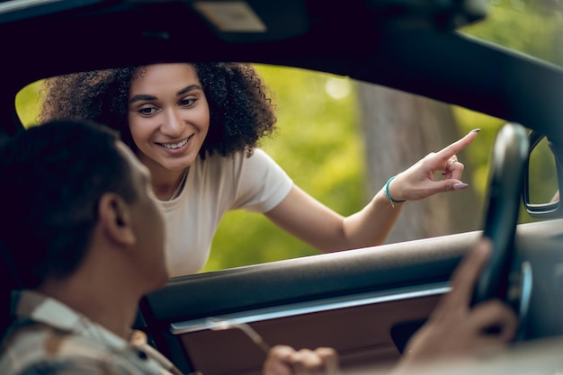 Photo young woman showing the way to a car driver and smiling