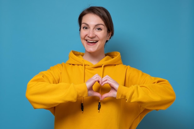 A young woman shows heart symbol on the chest with her hands. Studio shot