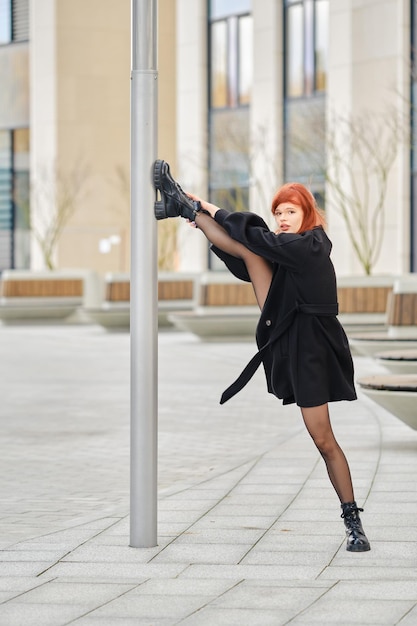 Young woman shows splits by putting her foot on a lamppost