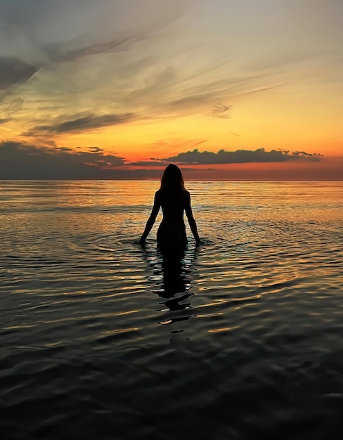 海の水の波とピンクの曇り空でオレンジ色の夕日で若い女性のシルエット