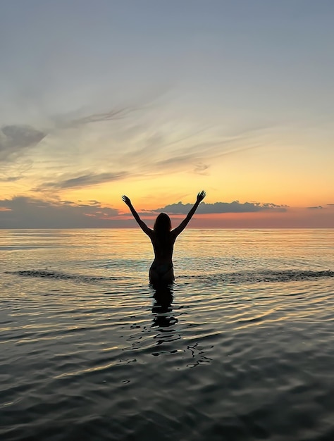 young woman  silhouette at orange sunset in the sea water wave and pink cloudy sky