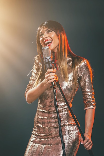 A young woman singer in front of the microphone. Sing with mouth wide open and with an expression of happiness on her face.