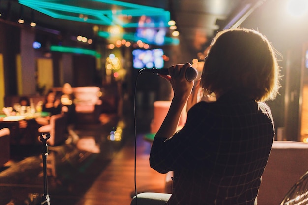 Photo young woman singing in karaoke and holding a microphone closeup singer at a party or concert on the background of a luminous star and smoke