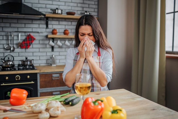 Фото Молодая женщина сидит за столом на кухне и чихает