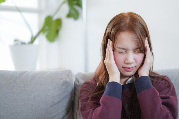 젊은 여자는 소파에 아픈 느낌과 두통에 앉아