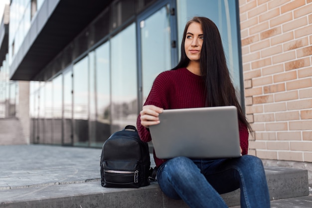 Young woman sit on urban stairs and work with laptop on the street