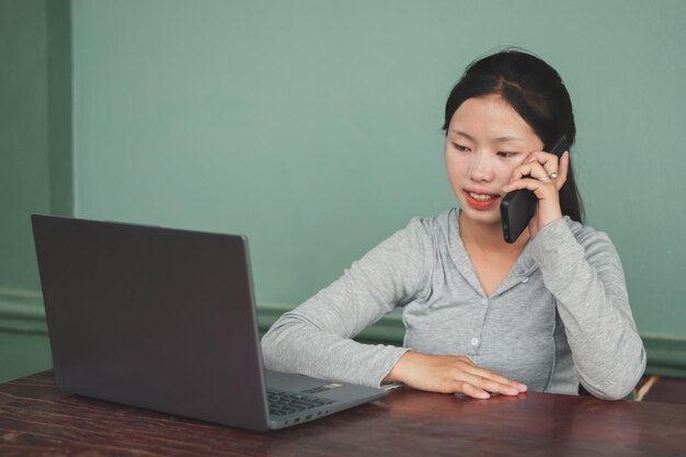 Photo a young woman siting on the desk at home and calling her customer than looking laptop screen small business at home and online communication social media concept copy space for individual text