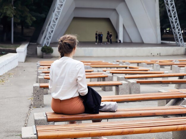 Young woman sits back on bench in front of concert scene, where rehearsal