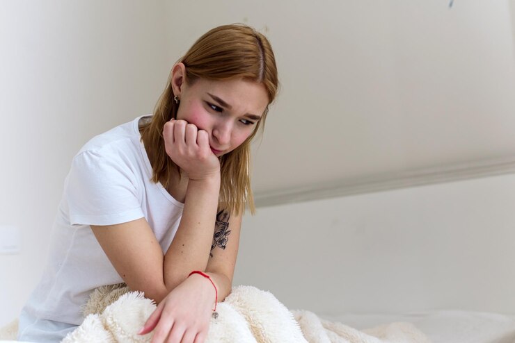 A young woman sits on the bed, holds her head in her hands and is sad. Depression at home. Headache.