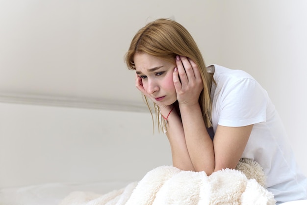 A young woman sits on the bed holds her head in her hands and\
is sad depression at home headache