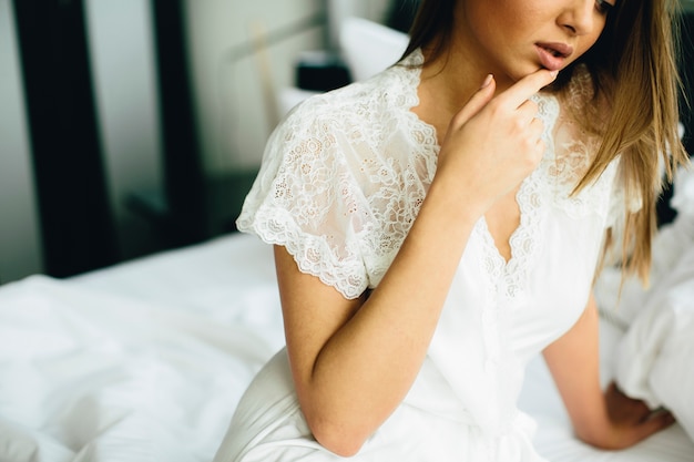 Foto la giovane donna si siede su un letto con tela bianca