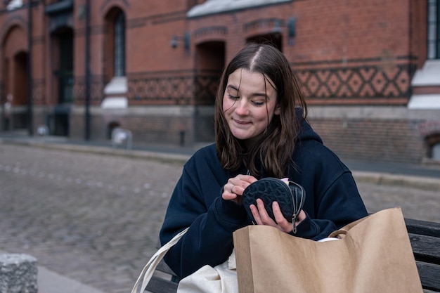 若い女性は、買い物の概念を財布と一緒にベンチに座っています