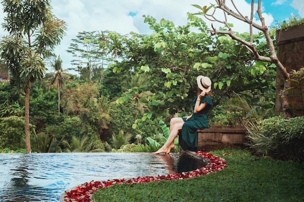 젊은 여자가 열대 정글, 우붓이 내려다 보이는 열린 개인 수영장 옆에 앉아
