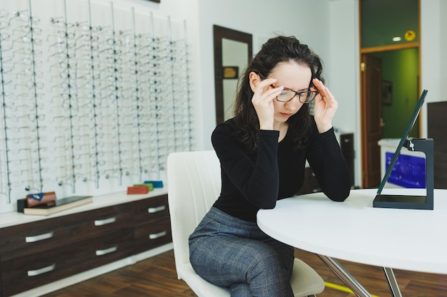 A young woman sits and chooses glasses in an ophthalmology salon Bad eyesight