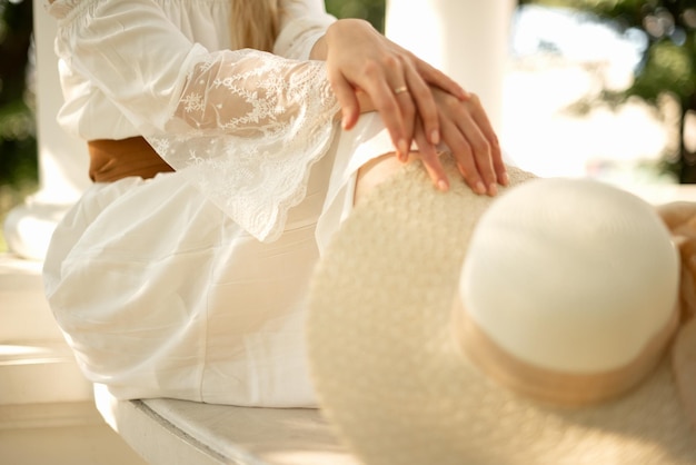 Young woman sits crossed her hand on knee and holding straw hat summer outdoor lifestyle