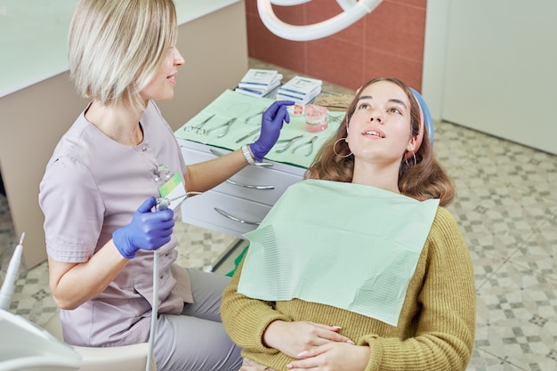 Una giovane donna si siede su una poltrona del dentista nell'ufficio della clinica odontoiatrica. medico e paziente di sesso femminile.